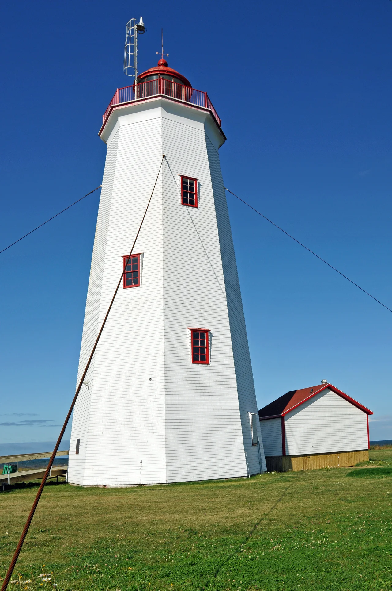 Miscou Island Lighthouse
This lighthouse was built in 1856 at the southern entrance to Chaleur Bay by Quebec Trinity House, which then supervices navigation on the St. Lawrence River and Gulf. Considered a major coastal aid it merited the subsequent installation of a powerful dioptric light and a diaphone fog alarm. The octagonal tower of hand-sawn timbers, shingled on the outside, was originally 74 feet in height and was extended in 1903 to 80 feet. This lighthouse, substantially in its original state, is among the oldest in the Gulf of St. Lawrence region.

The lantern at Miscou Island houses a functioning third-order Fresnel lens, the only Fresnel lens still operating in an authentic lighthouse in New Brunswick. After an environmental cleanup in 2008, the province undertook a large scale project to make this a major tourist destination in the region. A paved parking area (large enough for tour buses), a deck around the lighthouse and washroom facilities in addition to a large grass area are completed.